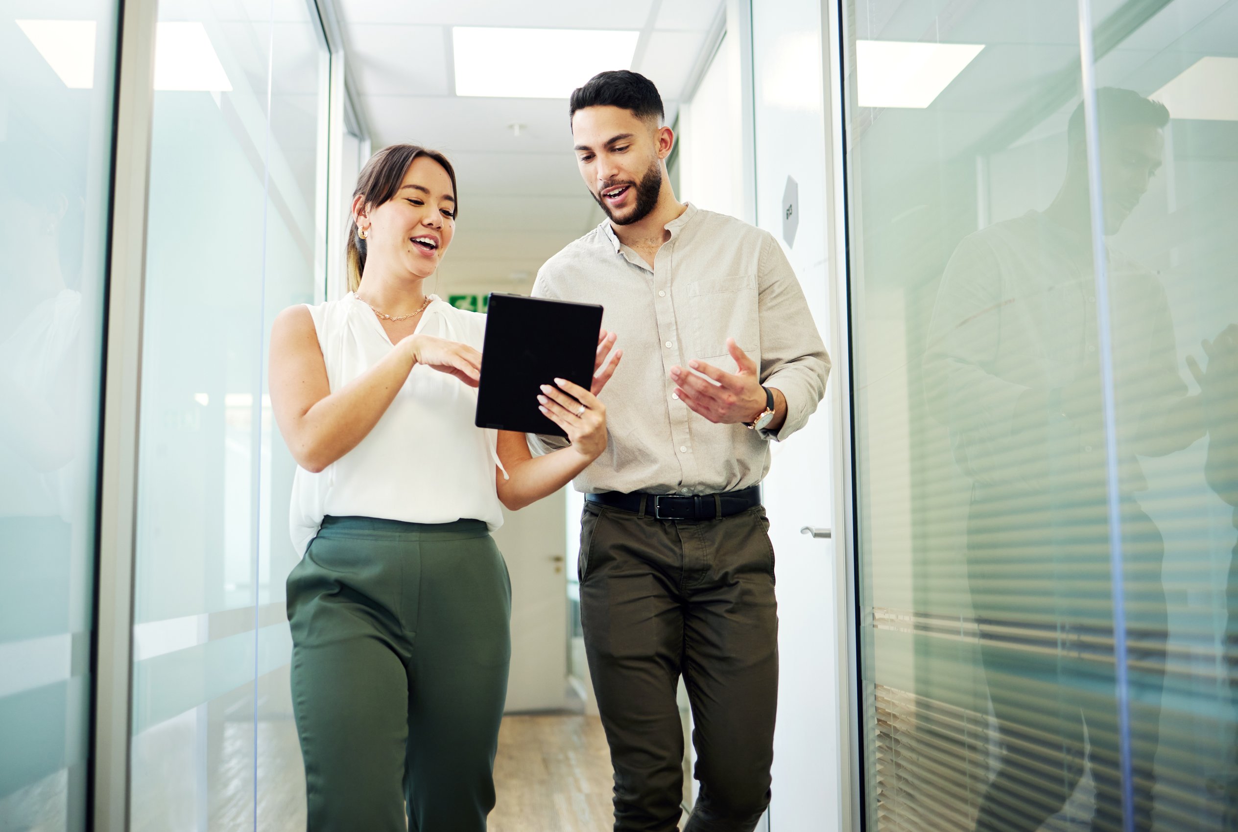 man and woman walking in a workplace hallway looking a tablet
