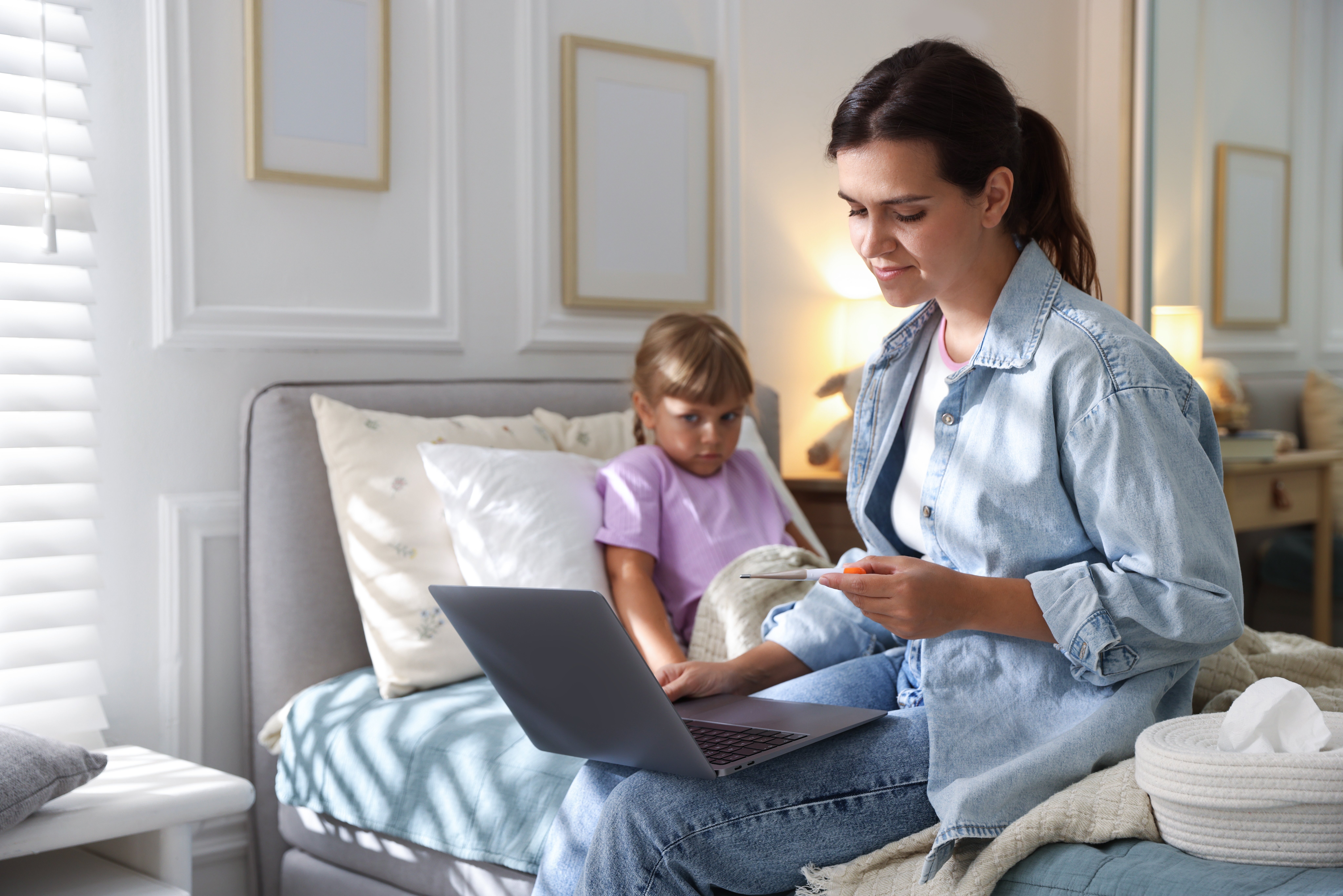 Mom taking her child's temperature while holding her laptop